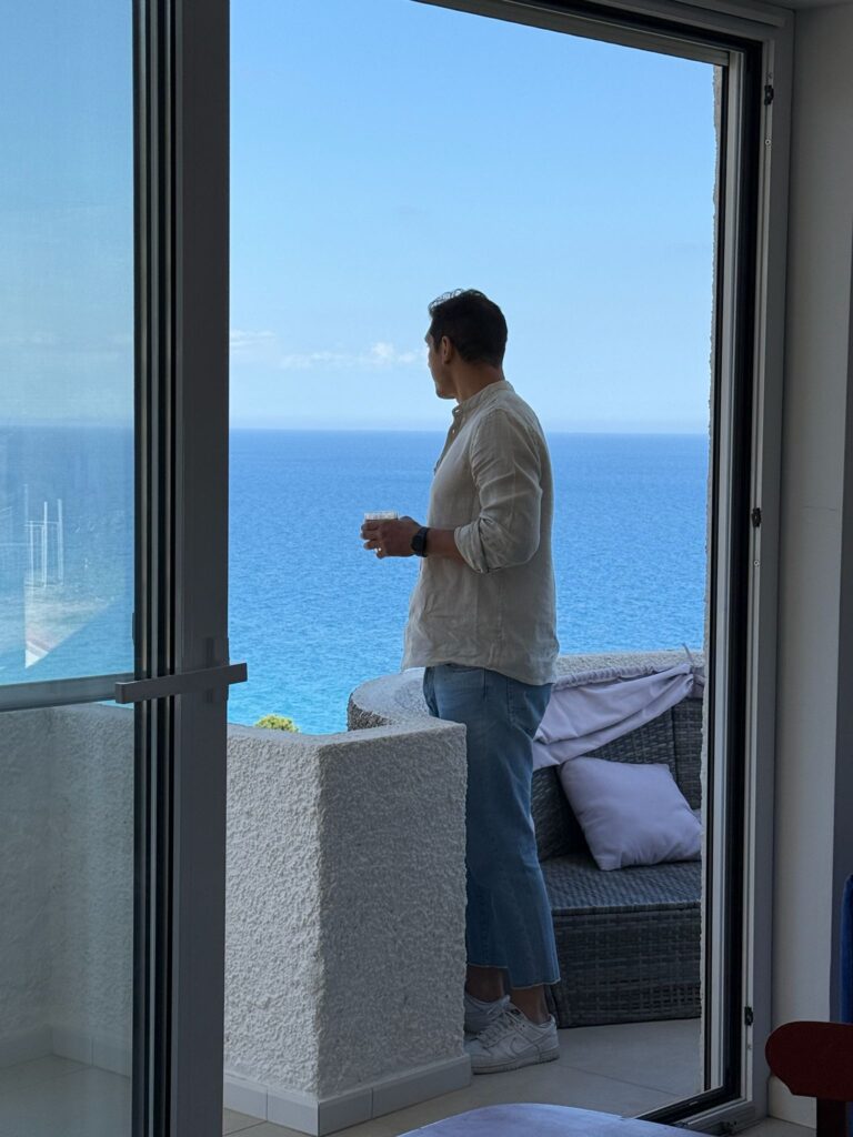 Man standing on a balcony overlooking the Calabrian sea, holding a drink.