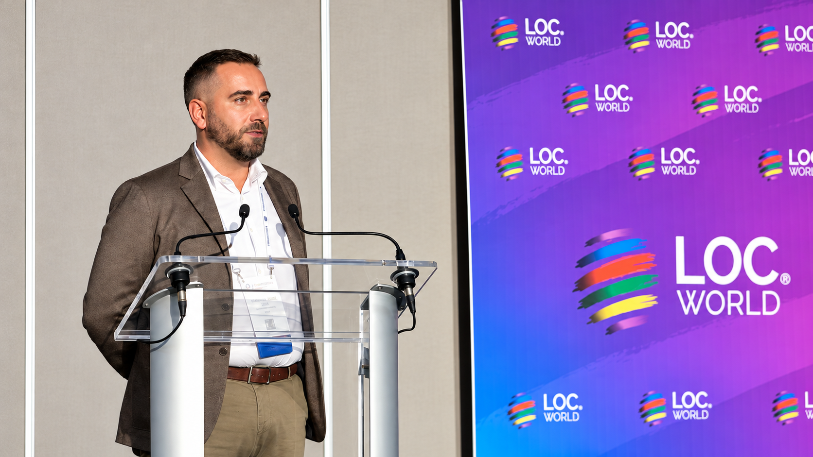 Anthony Neal Macri speaking behind a lectern beside the LocWorld banner in Vancouver.
